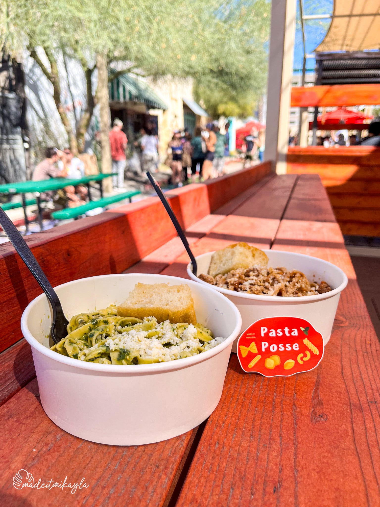 Two bowls of pasta on a wooden table with 'Pasta Posse' sticker in an outdoor setting.